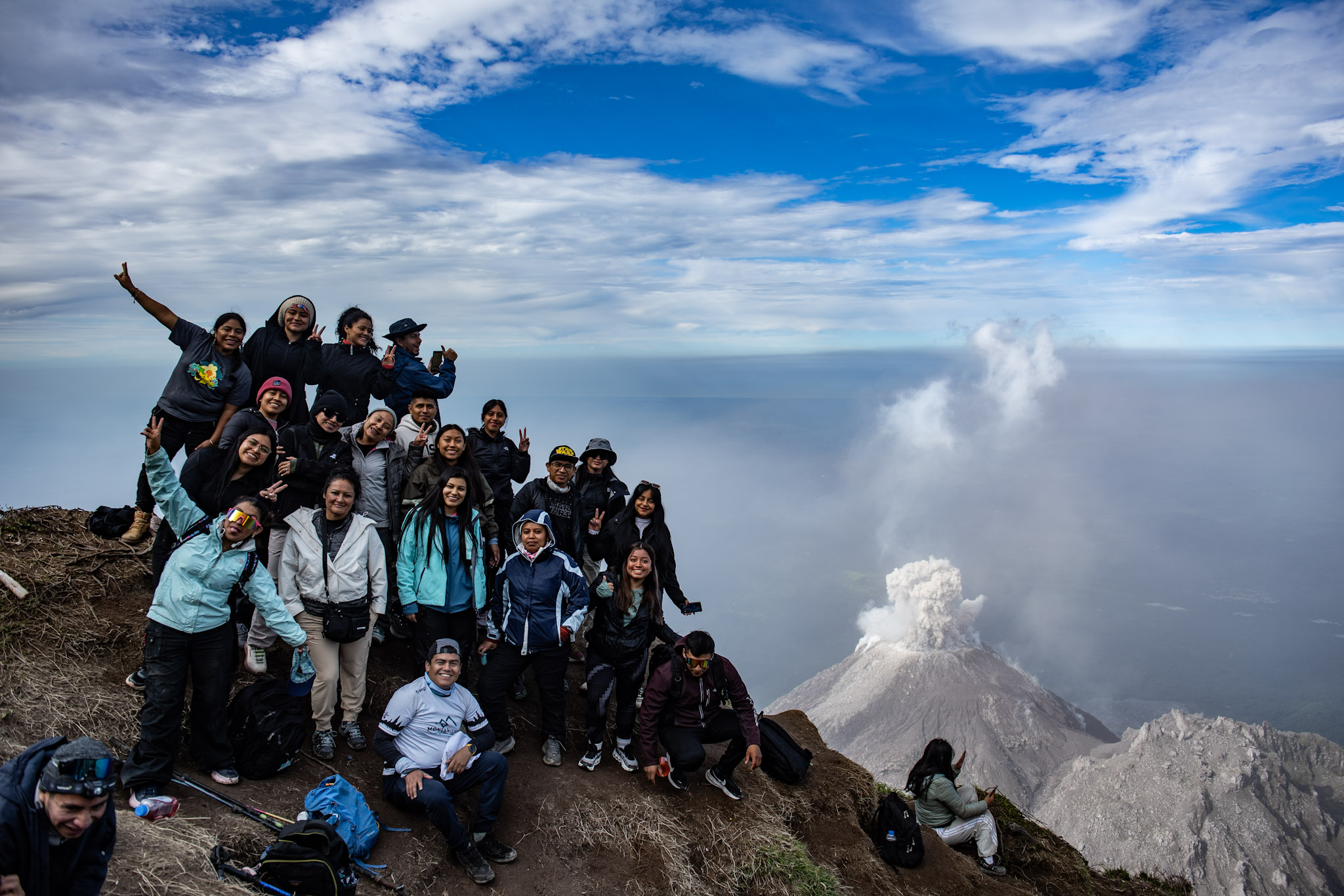 A group photo on El Pikacho with Santiaguito erupting in the background.